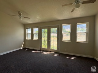 Spare room with ceiling fan, healthy amount of natural light, dark colored carpet, and vaulted ceiling