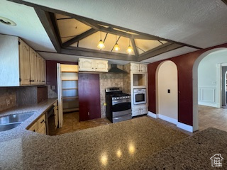 Kitchen featuring stainless steel stove, wall oven, arched walkways, ventilation hood, and dishwasher