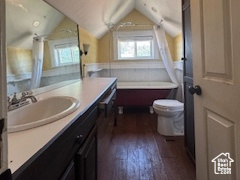 Bathroom with vaulted ceiling, hardwood / wood-style floors, vanity, a bathtub, and track lighting