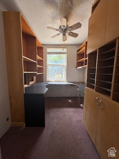Home office featuring built in desk, ceiling fan, dark carpet, and a textured ceiling