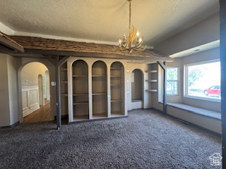 Carpeted empty room with arched walkways, a chandelier, and a textured ceiling