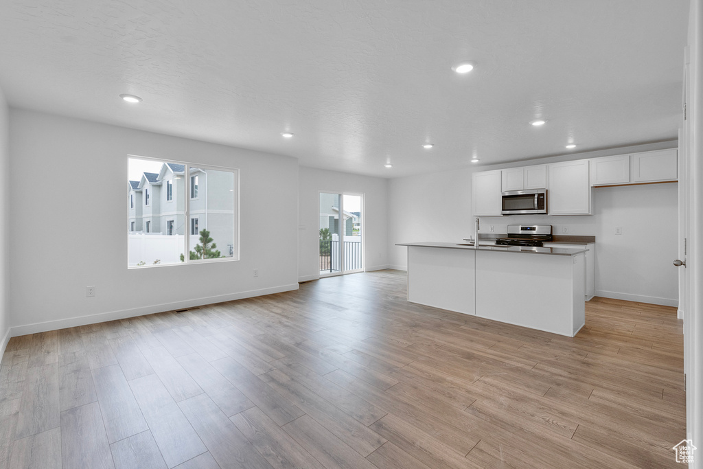 Kitchen featuring appliances with stainless steel finishes, open floor plan, white cabinetry, light wood-style floors, and recessed lighting