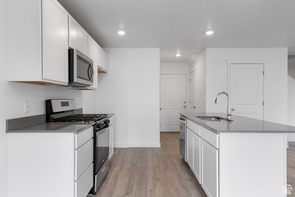 Kitchen with appliances with stainless steel finishes, light wood-style flooring, a kitchen island with sink, white cabinets, and recessed lighting
