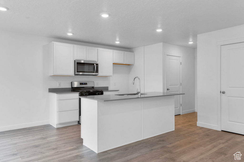 Kitchen featuring stainless steel microwave, range, light wood-style floors, white cabinetry, and recessed lighting