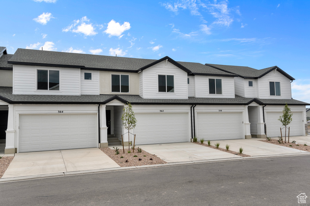 Multi unit property with an attached garage, driveway, and roof with shingles