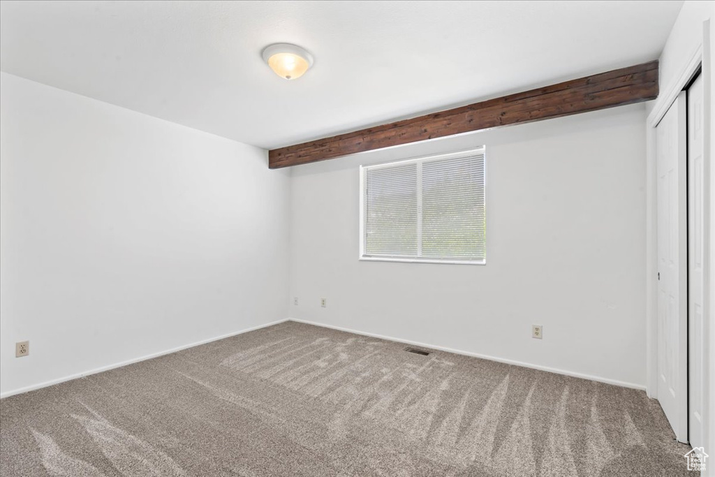 Spare room featuring carpet floors and beam ceiling