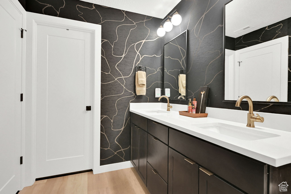Bathroom with double vanity, wood finished floors, and wallpapered walls