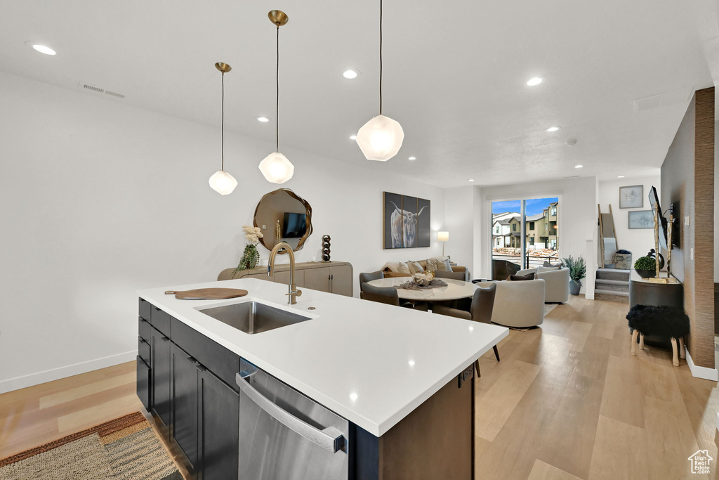 Kitchen with stainless steel dishwasher, light wood finished floors, light countertops, recessed lighting, and an island with sink