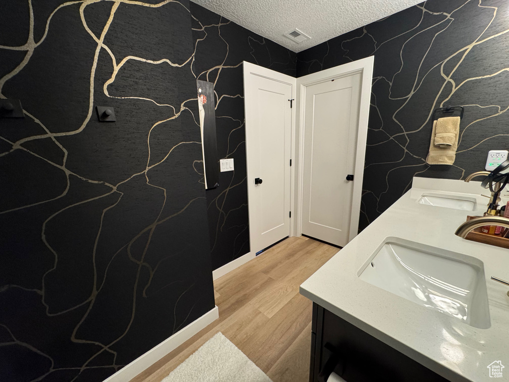 Bathroom with wallpapered walls, double vanity, wood finished floors, and a textured ceiling
