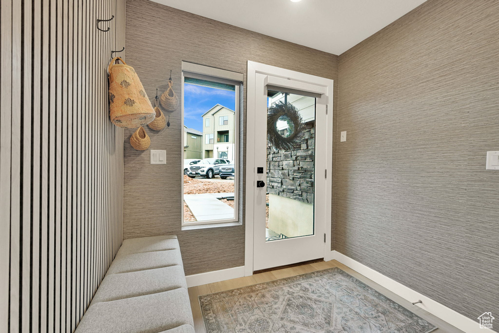 Doorway to outside with wood finished floors and wallpapered walls