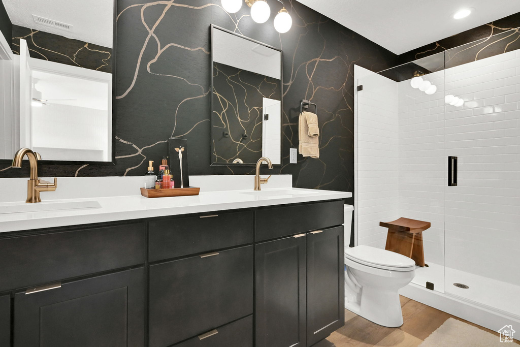 Full bath featuring double vanity, wood finished floors, wallpapered walls, and a tile shower