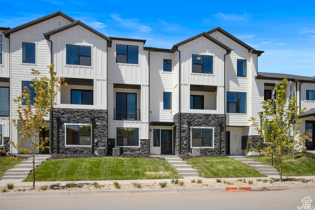 Townhome / multi-family property with stone siding, board and batten siding, and a front lawn
