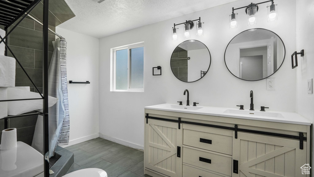 Bathroom with double vanity, tiled shower, a textured ceiling, and wood finished floors