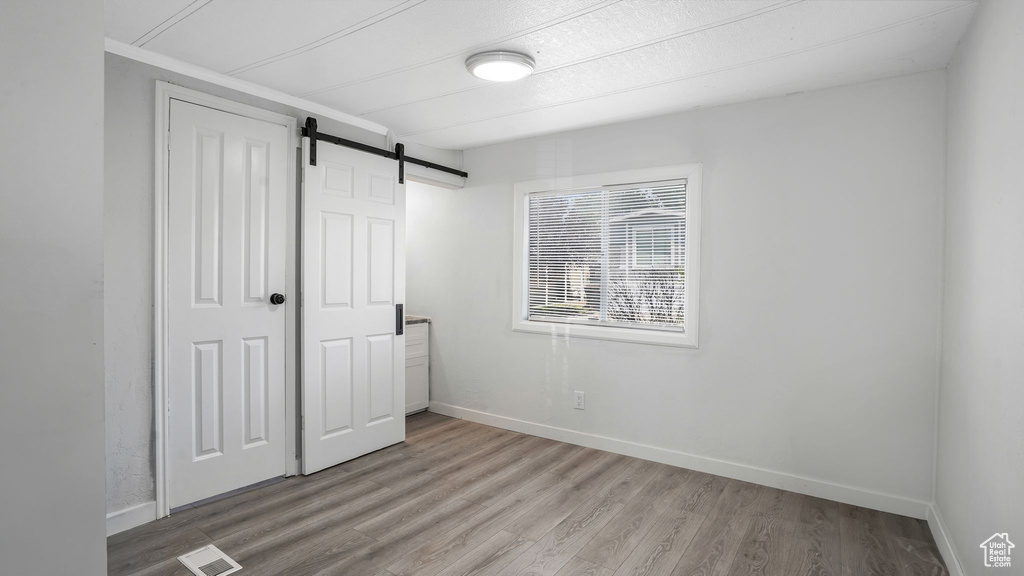 Unfurnished bedroom with light wood-type flooring, a barn door, and a closet