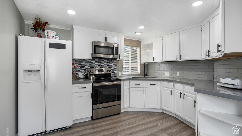 Kitchen with stainless steel appliances, open shelves, white cabinets, dark countertops, and recessed lighting