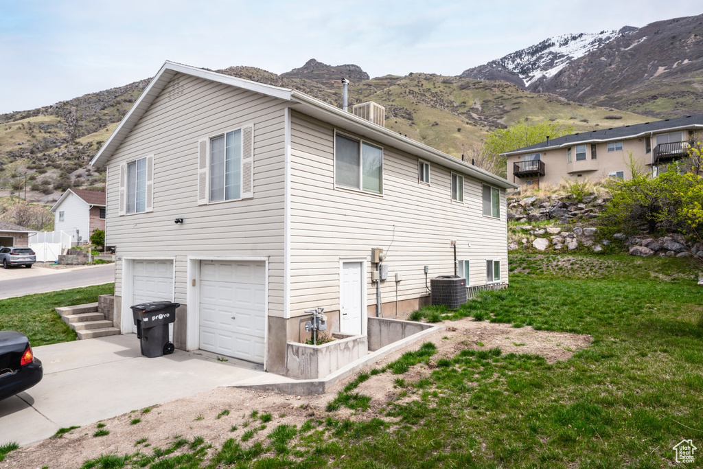 View of property exterior with a mountain view, a garage, driveway, and central AC