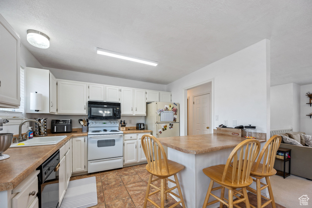 Kitchen featuring a sink, a kitchen bar, a peninsula, black appliances, and white cabinetry