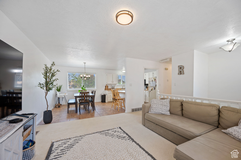 Living room with baseboards, light carpet, a chandelier, a textured ceiling, and visible vents
