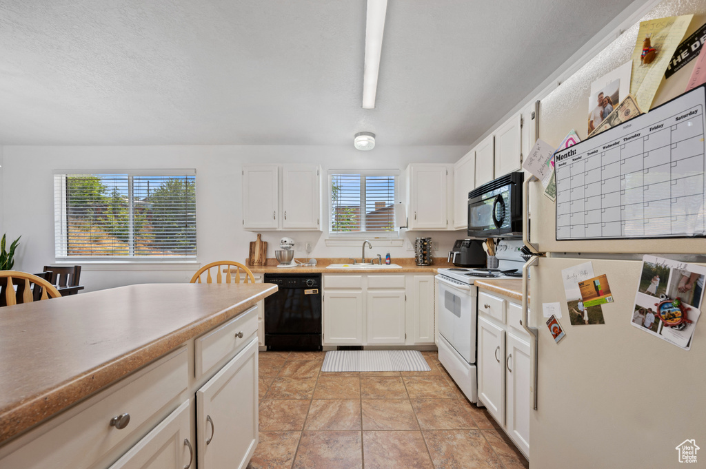 Kitchen featuring a sink, light countertops, black appliances, and white cabinetry