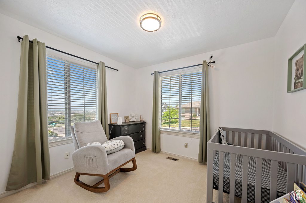 Bedroom with a crib, visible vents, multiple windows, and light colored carpet