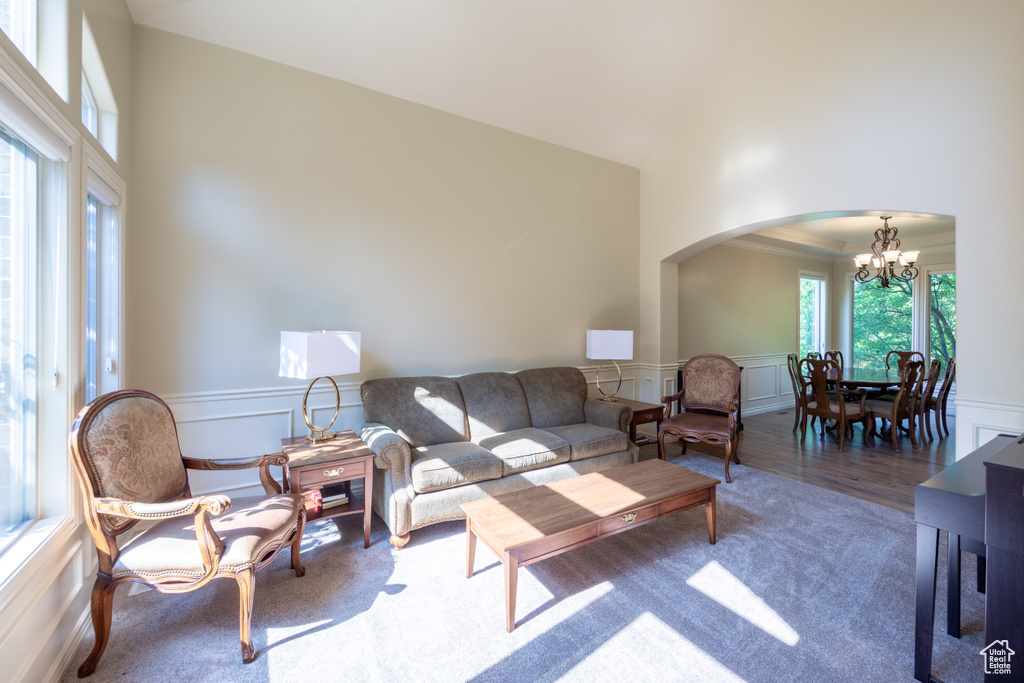 Carpeted living area featuring arched walkways, high vaulted ceiling, a chandelier, a decorative wall, and a wainscoted wall