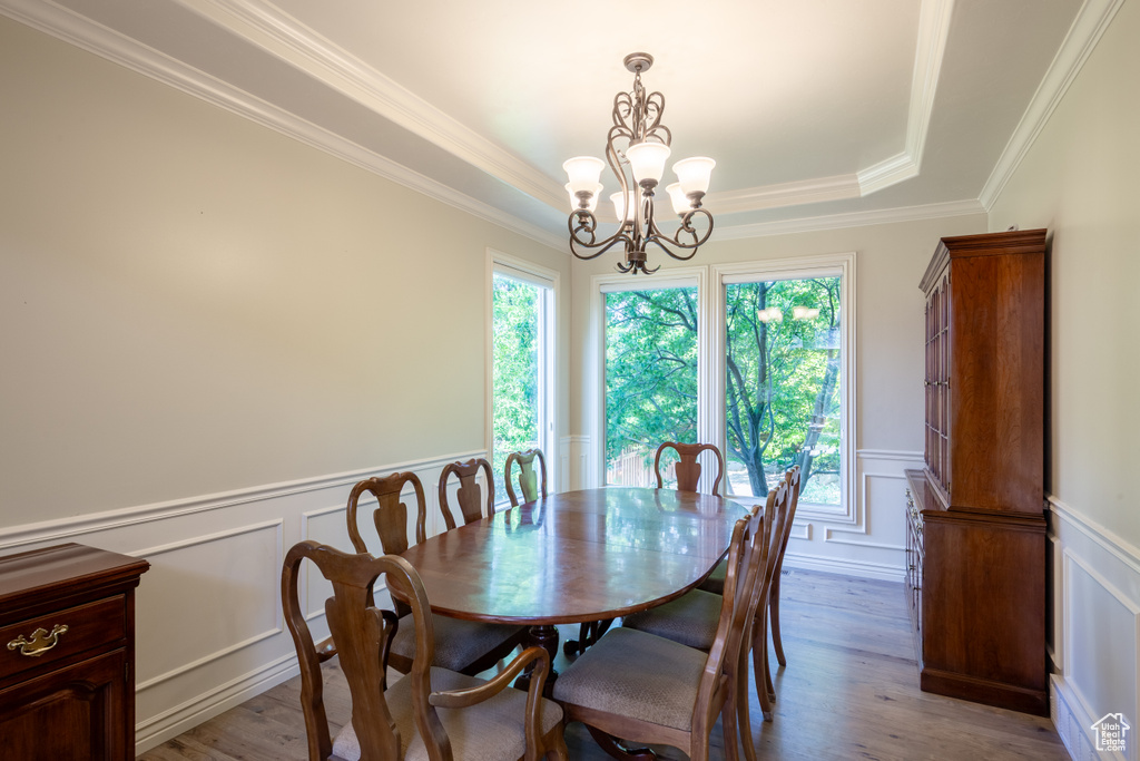 Dining room with a chandelier, a decorative wall, light wood finished floors, wainscoting, and a tray ceiling