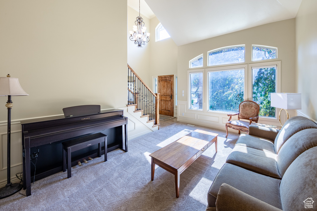 Carpeted living area with high vaulted ceiling, a chandelier, stairway, and a wainscoted wall