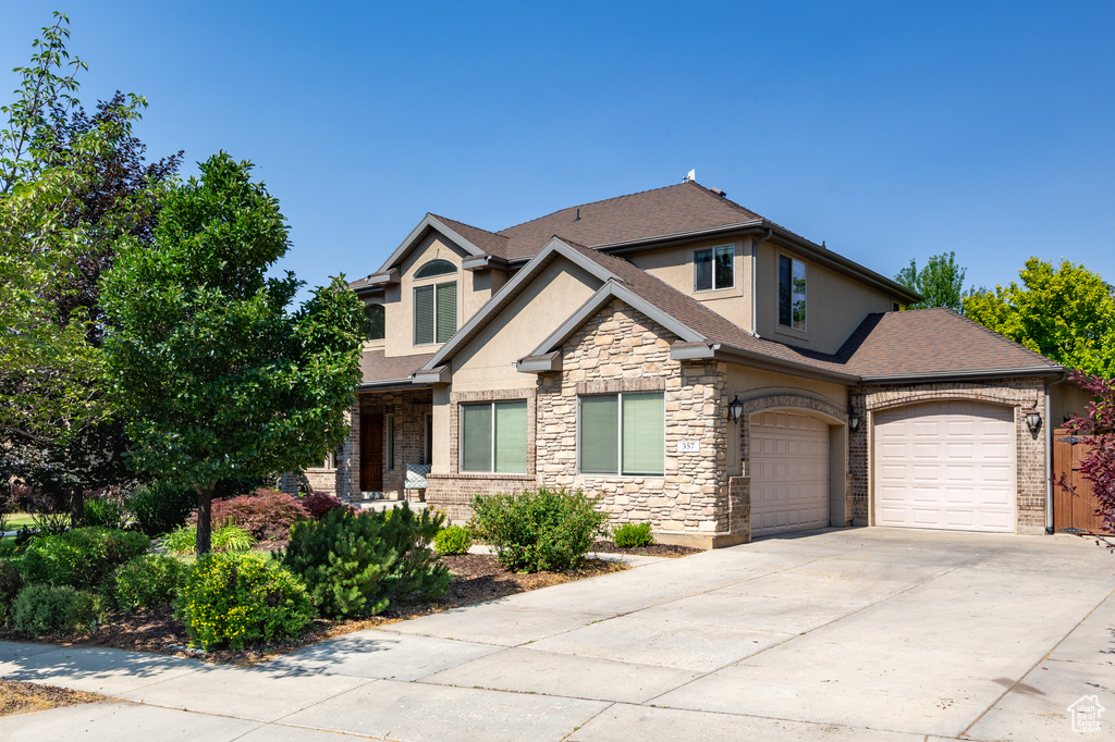 View of front facade featuring stucco siding, stone siding, a garage, driveway, and a shingled roof