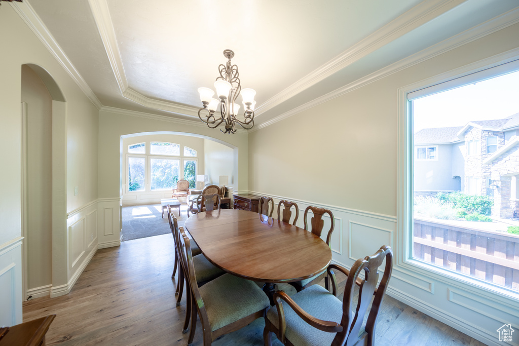 Dining area with arched walkways, light wood-type flooring, a decorative wall, crown molding, and a tray ceiling