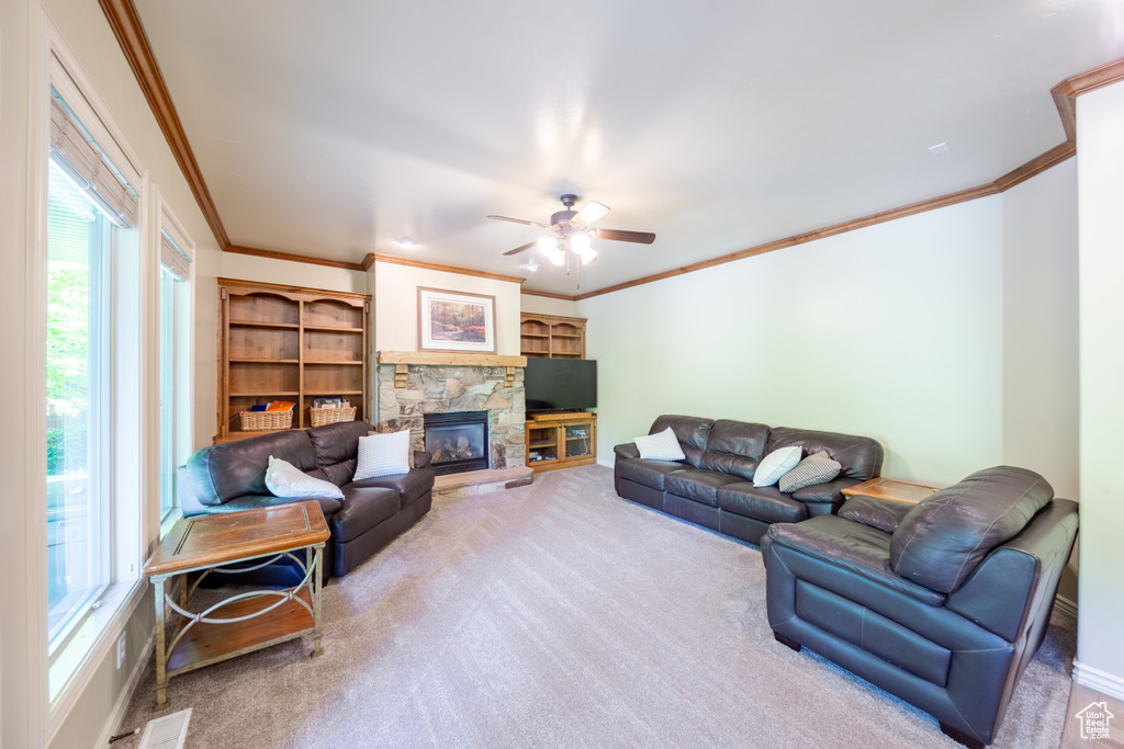 Carpeted living room featuring ornamental molding, a ceiling fan, and a stone fireplace