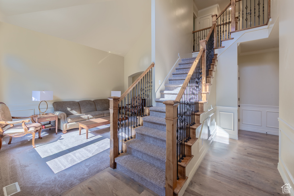 Staircase with wood finished floors, a high ceiling, crown molding, a decorative wall, and wainscoting
