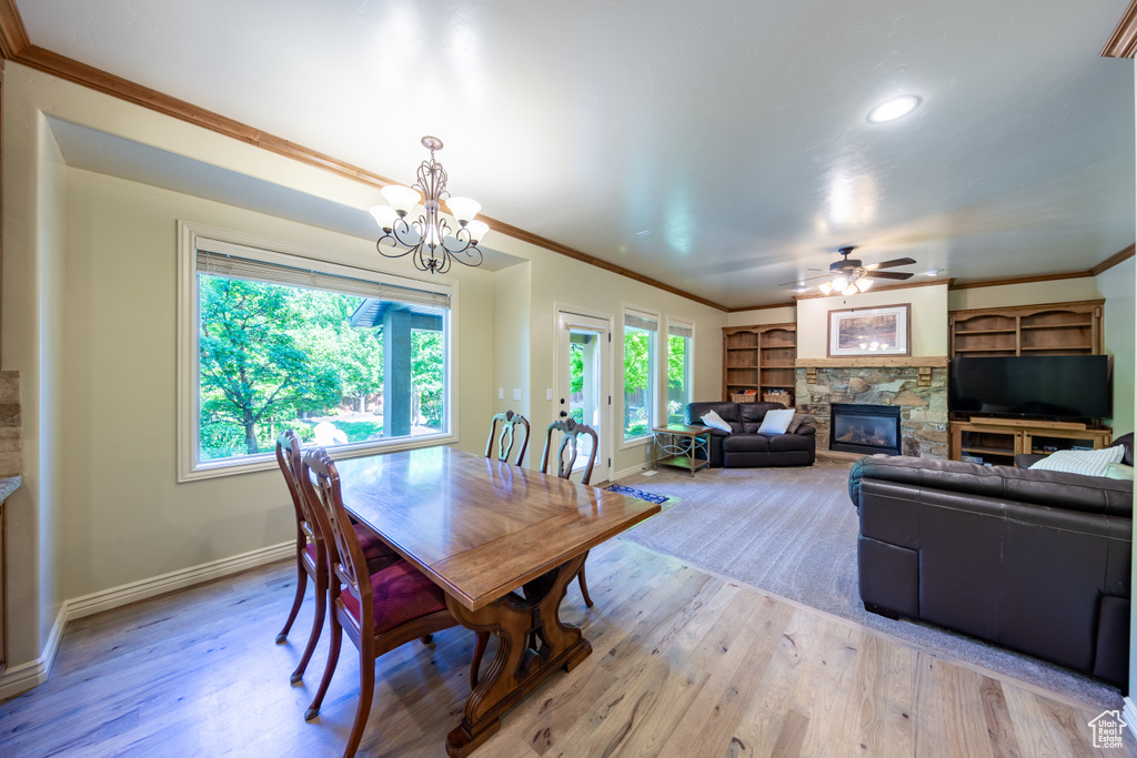 Dining space with a stone fireplace, plenty of natural light, ornamental molding, light wood finished floors, and recessed lighting