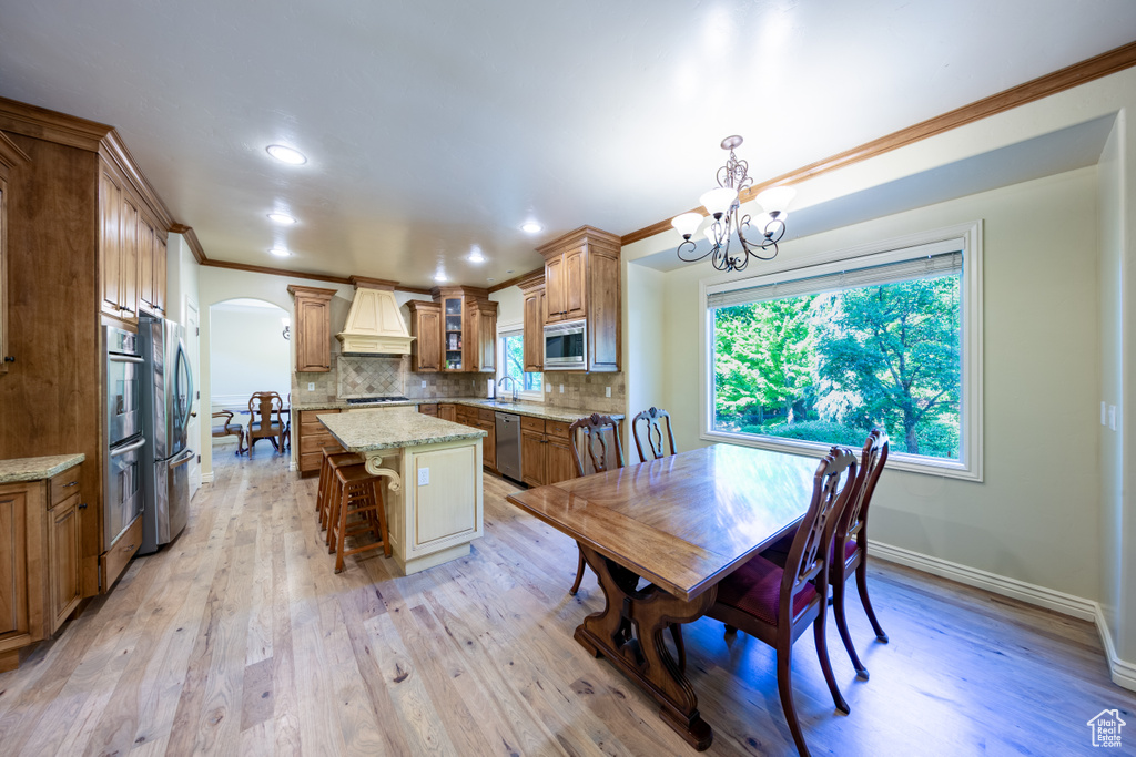 Dining room with arched walkways, a chandelier, crown molding, light wood finished floors, and recessed lighting