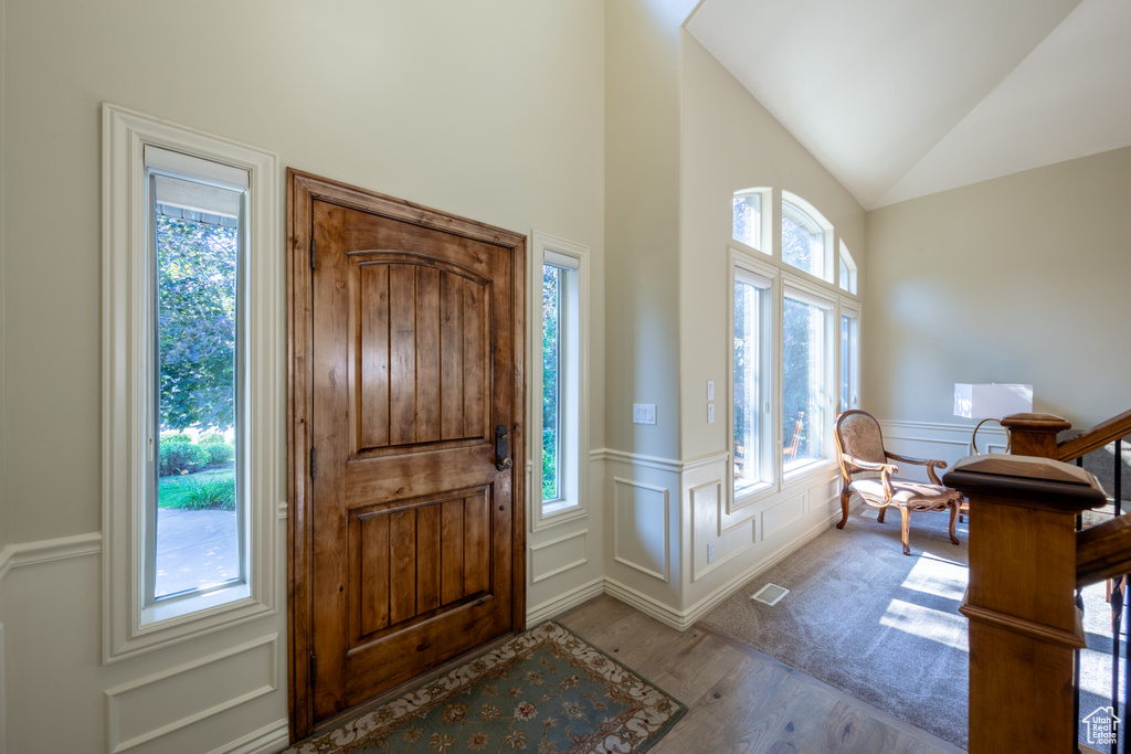Foyer entrance featuring wood finished floors, a decorative wall, a wainscoted wall, and lofted ceiling