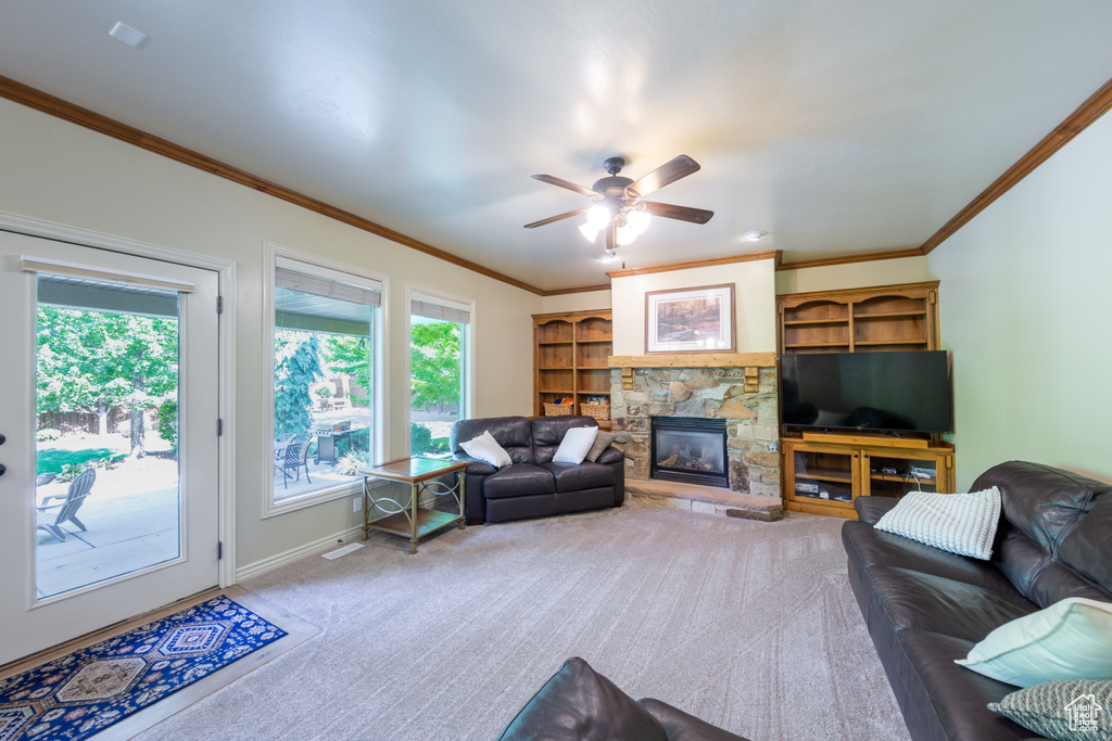 Carpeted living area featuring ornamental molding, a stone fireplace, and ceiling fan