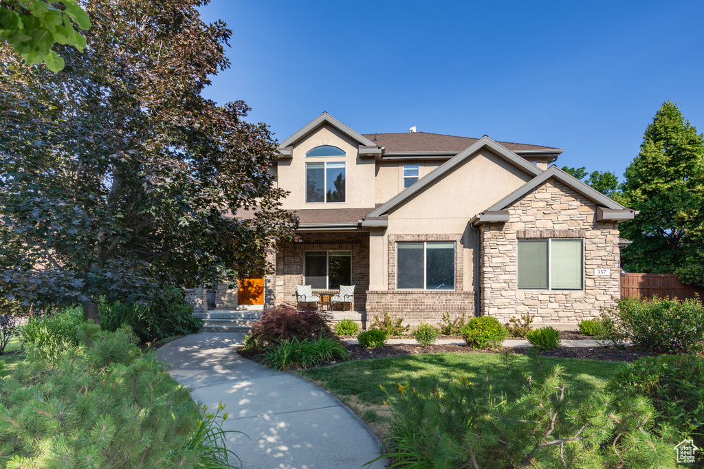 View of front of home featuring stucco siding, covered porch, and stone siding