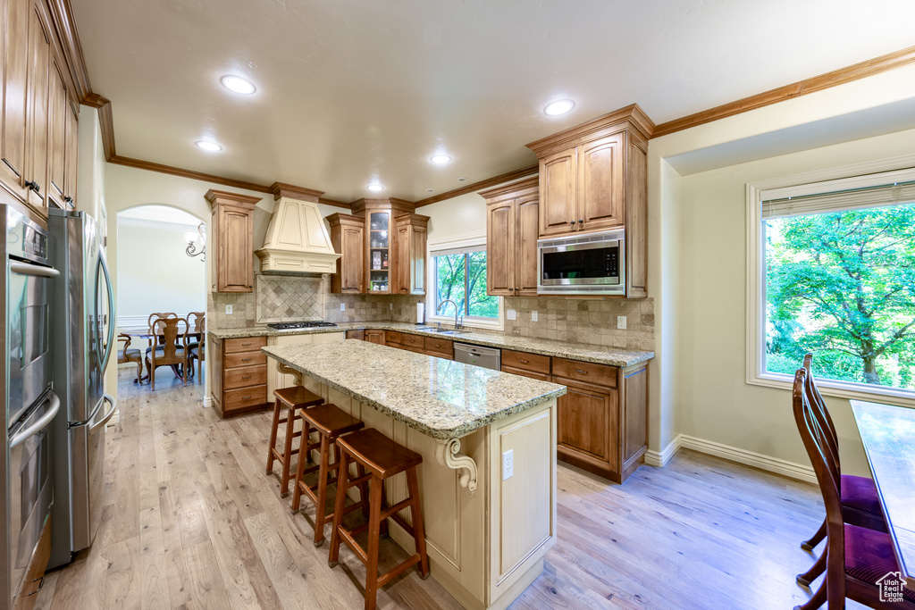 Kitchen with appliances with stainless steel finishes, premium range hood, crown molding, arched walkways, and a breakfast bar