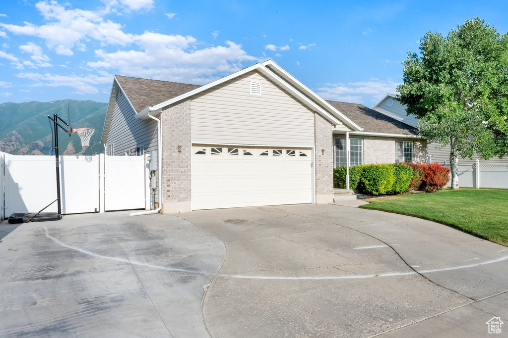 Ranch-style house featuring brick siding, concrete driveway, an attached garage, a mountain view, and a gate