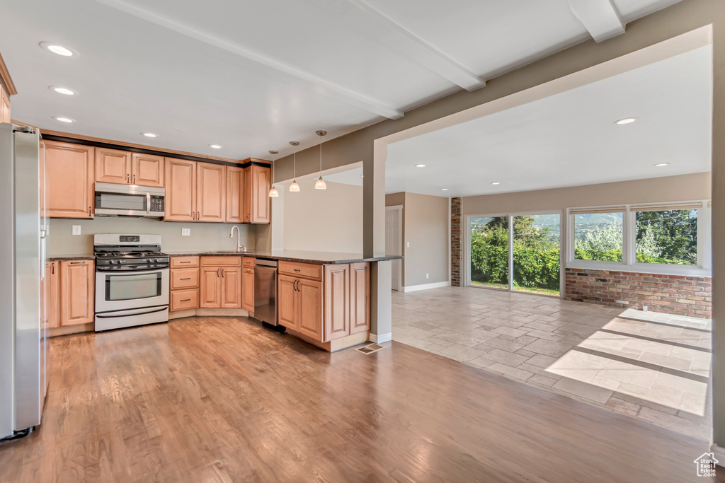 Kitchen with stainless steel appliances, a peninsula, recessed lighting, light brown cabinets, and decorative light fixtures