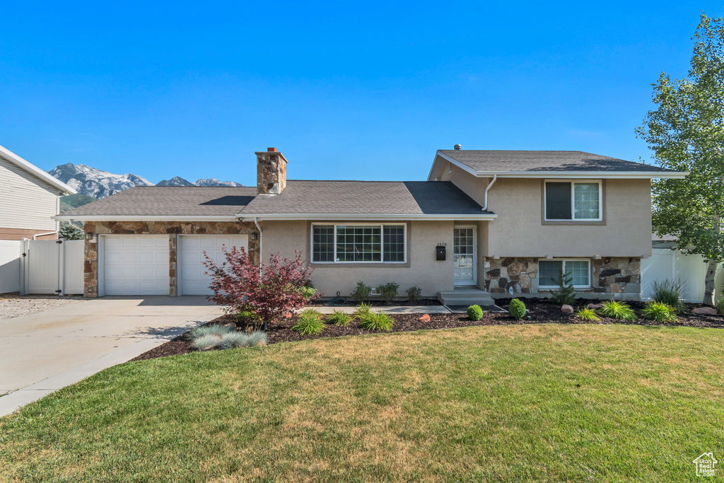 Tri-level home featuring stucco siding, a chimney, driveway, a garage, and stone siding