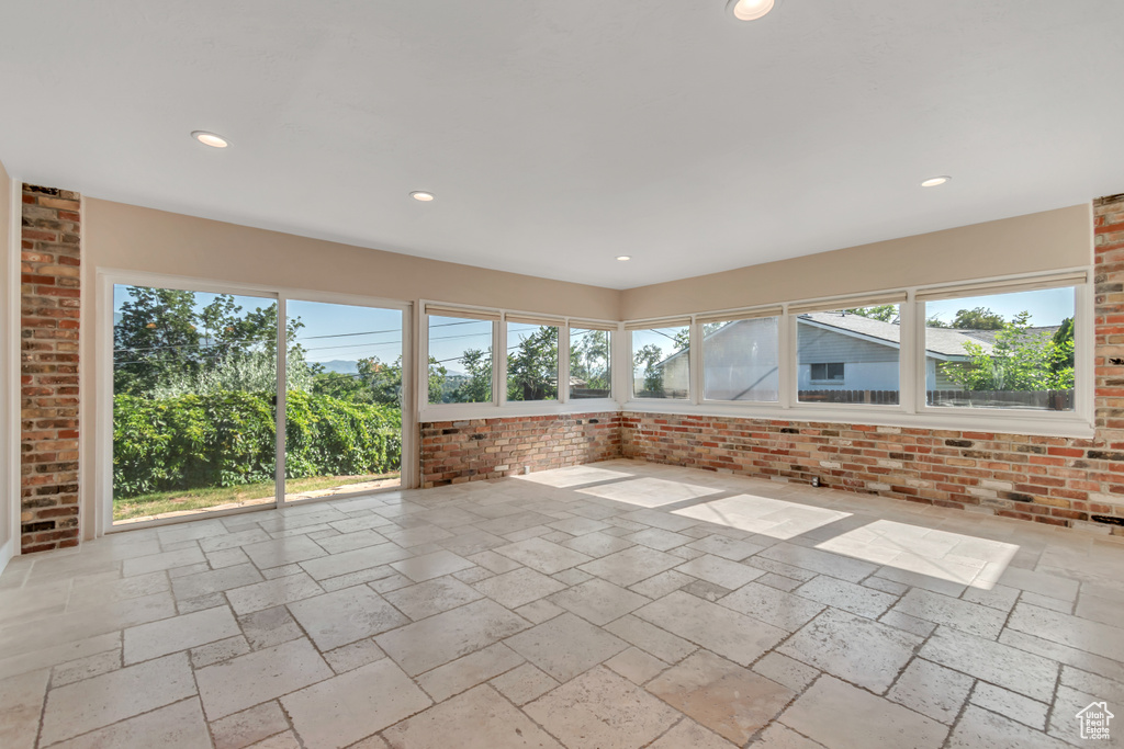 Unfurnished sunroom featuring stone tile floors, recessed lighting, and brick wall