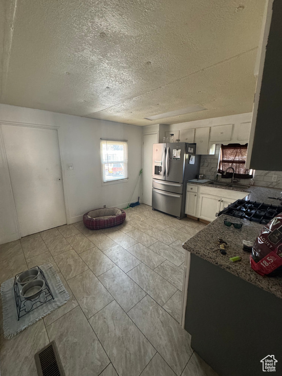 Kitchen with stainless steel fridge with ice dispenser, decorative backsplash, white cabinetry, a textured ceiling, and gas range oven