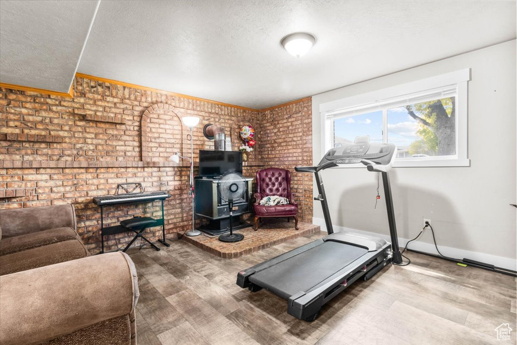 Workout area with a wood stove, brick wall, wood finished floors, and a textured ceiling