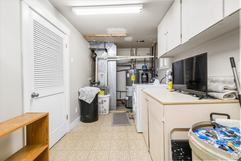 Laundry area with gas water heater, light flooring, cabinet space, and heating unit