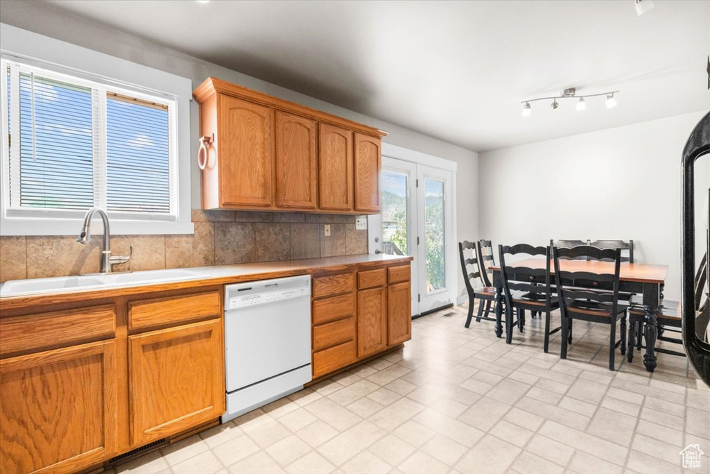 Kitchen featuring dishwasher, brown cabinetry, light countertops, backsplash, and rail lighting