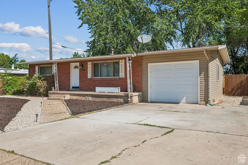 Ranch-style home with an attached garage, concrete driveway, brick siding, and a porch
