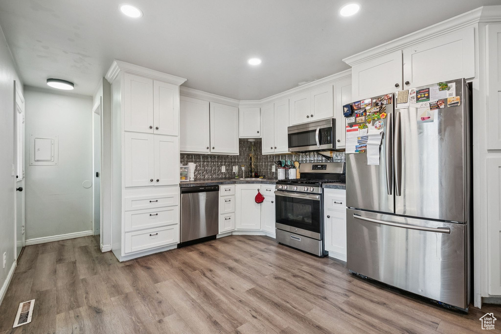Kitchen with stainless steel appliances, white cabinets, dark countertops, light wood-style flooring, and decorative backsplash