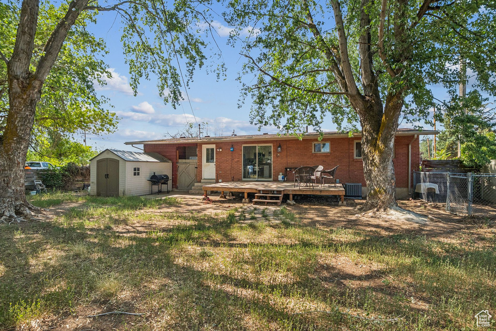Rear view of house with a storage unit, a wooden deck, and brick siding