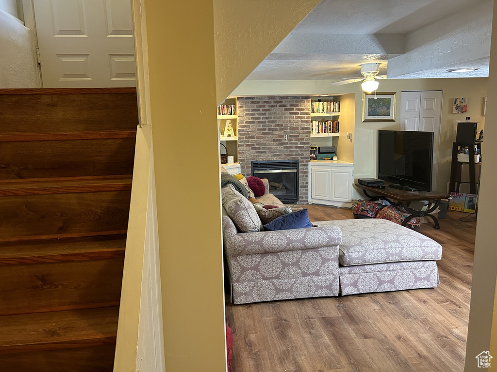 Living area with a fireplace, wood finished floors, ceiling fan, and built in features