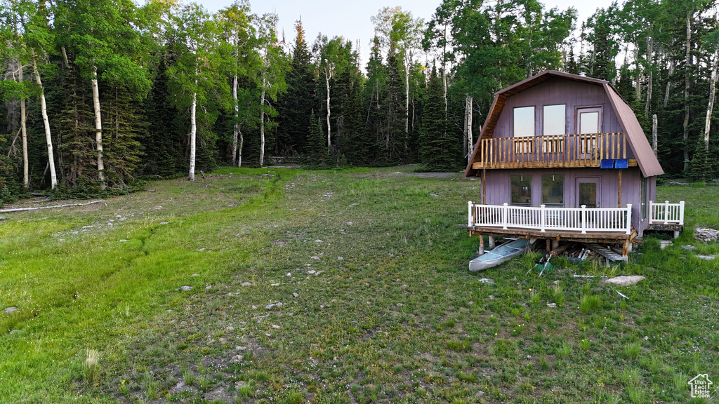 Back of property with a gambrel roof, a deck, a yard, and a forest view
